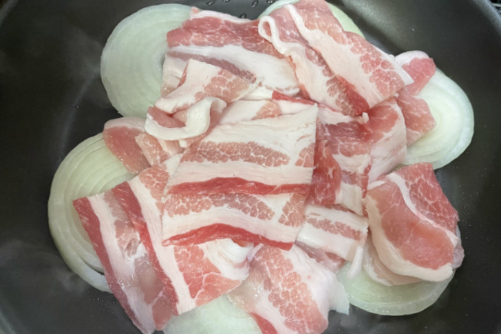 輪切りの新玉ねぎと豚バラ肉をフライパンで炒める